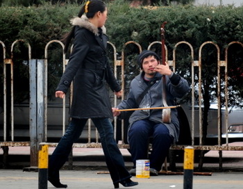 Стильно одетая молодая женщина проходит мимо бедного человека, играющего на музыкальном инструменте на китайской улице. Коэффициент Джини в Китае, который измеряет неравенство доходов, в течение последних двух лет составлял 0,6, что намного превышает международный уровень тревоги (0,4). Фото: Frederic J. Brown/AFP/Getty Images